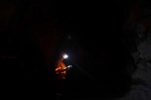 Man With Illuminated Headlamp In Dark Cave